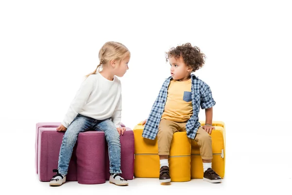 Multicultural irritated kids sitting on puzzle chairs, on white — Stock Photo