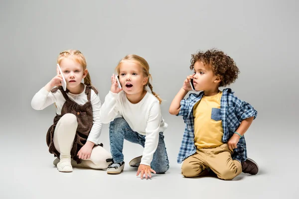 Adorable multicultural kids talking smartphones on grey — Stock Photo