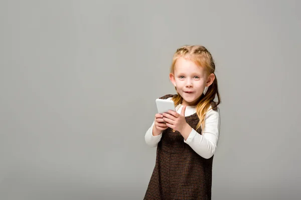 Niño sonriente usando teléfono inteligente, aislado en gris - foto de stock