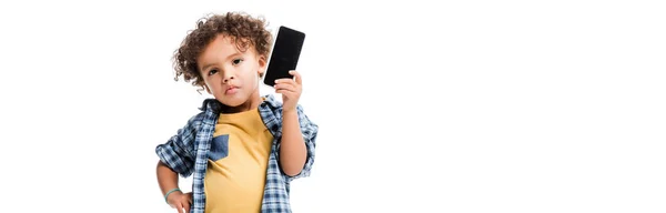 Plano panorámico de niño afroamericano pensativo sosteniendo teléfono inteligente con pantalla en blanco, aislado en blanco - foto de stock