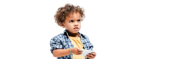 Tiro panorâmico de pouco menino americano africano irritado usando smartphone, isolado no branco — Fotografia de Stock