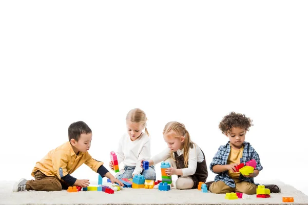 Multicultural children playing with wooden blocks on carpet, isolated on white — Stock Photo