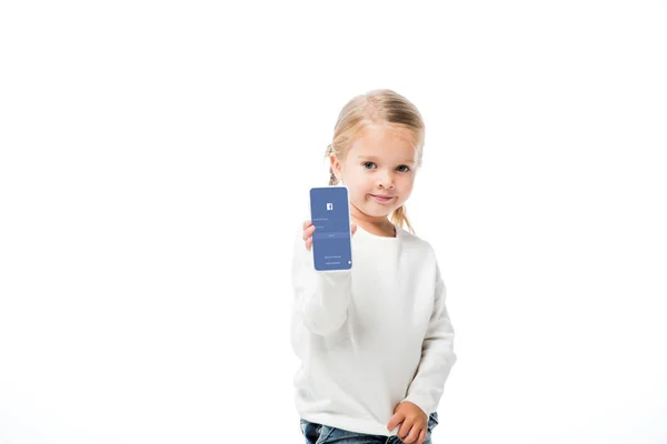 KYIV, UCRANIA - 18 de noviembre de 2019: niño adorable mostrando teléfono inteligente con aplicación de Facebook en la pantalla, aislado en blanco - foto de stock