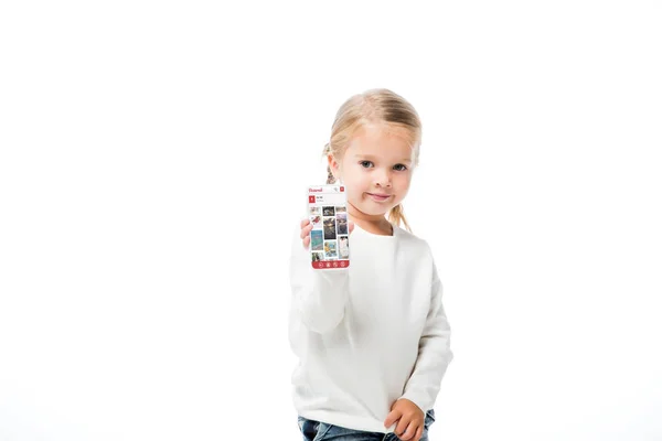 KYIV, UCRANIA - 18 de noviembre de 2019: niño adorable mostrando el teléfono inteligente con la aplicación pinterest en la pantalla, aislado en blanco - foto de stock