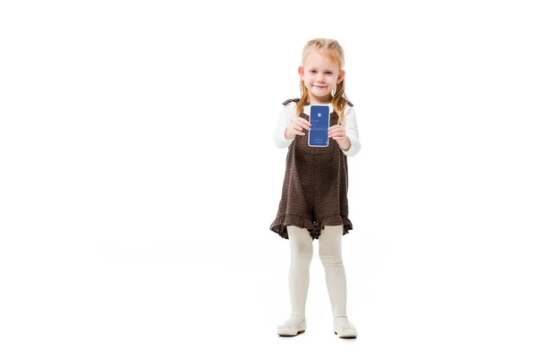 KYIV, UCRANIA - 18 de noviembre de 2019: niño adorable mostrando teléfono inteligente con aplicación de Facebook en la pantalla, aislado en blanco - foto de stock