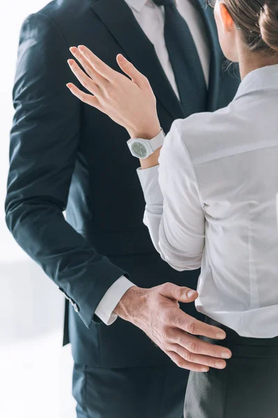 Recortado vista de hombre de negocios en traje abrazo secretario en la oficina - foto de stock