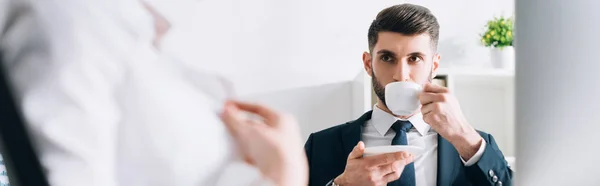 Plano panorámico de hombre de negocios tomando café y mirando a la secretaria en la oficina - foto de stock