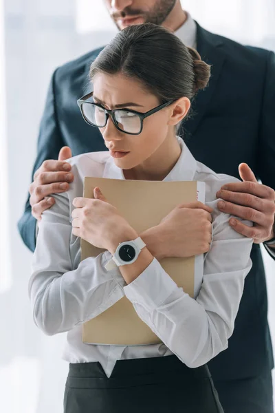 Cropped view of businessman hugging scared secretary in office — Stock Photo