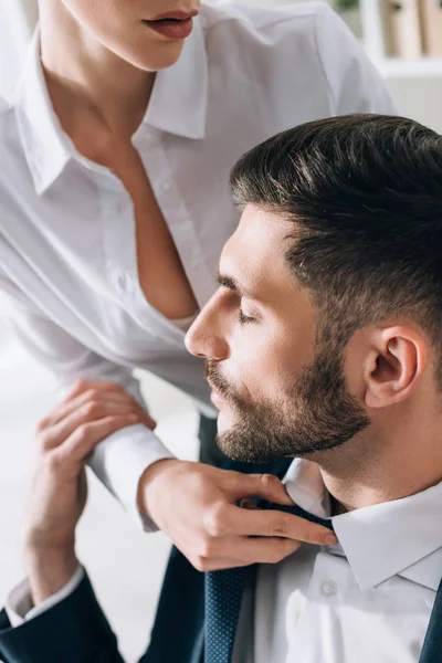 Cropped view of secretary with big breast pulling tie of businessman in office — Stock Photo