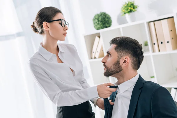 Attractive secretary pulling tie of handsome businessman in office — Stock Photo