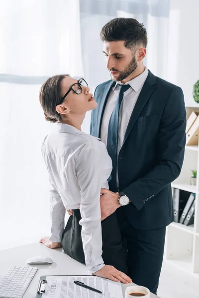 Bell'uomo d'affari che abbraccia attraente segretaria con gli occhi chiusi in ufficio — Foto stock