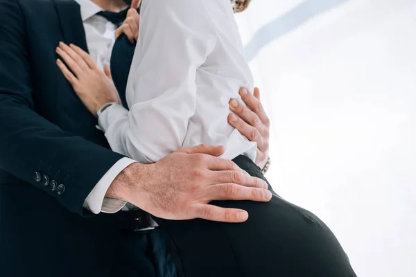 Recortado vista de hombre de negocios en traje abrazo secretario en la oficina - foto de stock