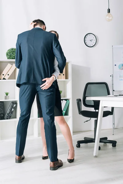 Rückseite des Geschäftsmannes im Anzug umarmt Sekretärin im Büro — Stockfoto