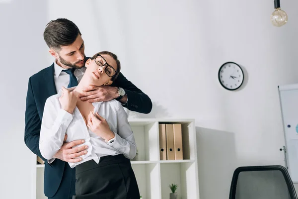 Guapo hombre de negocios abrazando sexy secretaria con los ojos cerrados en la oficina - foto de stock