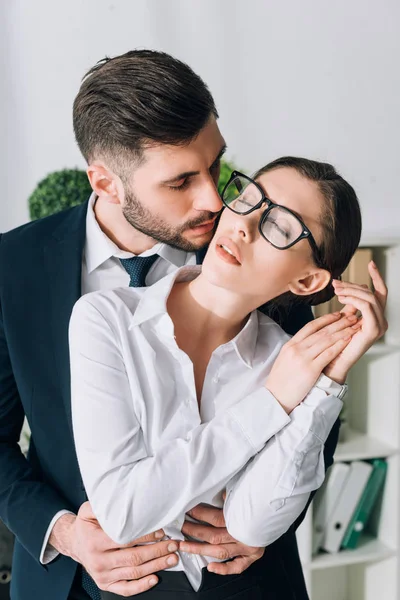 Handsome businessman hugging and kissing secretary in office — Stock Photo