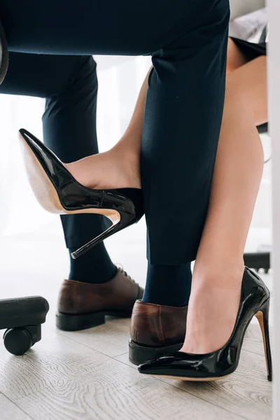 Vue recadrée de secrétaire en talons touchante jambe de l'homme d'affaires en fonction — Stock Photo