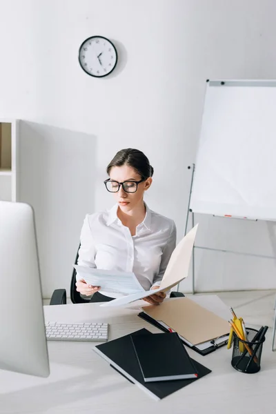 Atractiva mujer de negocios sentada en la mesa y haciendo papeleo - foto de stock