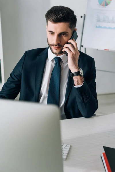 Бизнесмен сидит за столом и разговаривает на смартфоне в офисе — стоковое фото