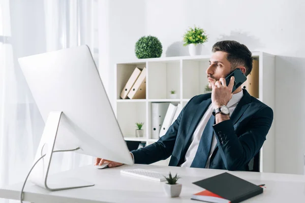 Businessman sitting at table and talking on smartphone in office — Stock Photo