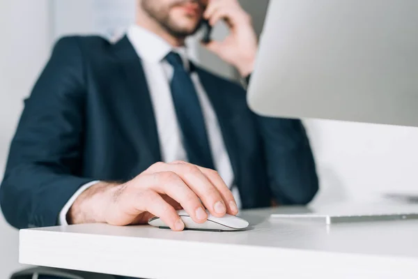 Vista recortada de hombre de negocios en traje sentado en la mesa y hablando en el teléfono inteligente - foto de stock