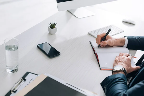 Vista ritagliata di uomo d'affari seduto a tavola e la scrittura in notebook — Foto stock