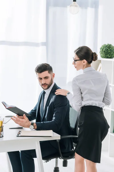 Секретарь трогает плечо привлекательного бизнесмена в офисе — стоковое фото