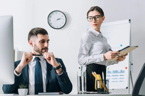 Handsome businessman sitting at table and looking at secretary in office — Stock Photo