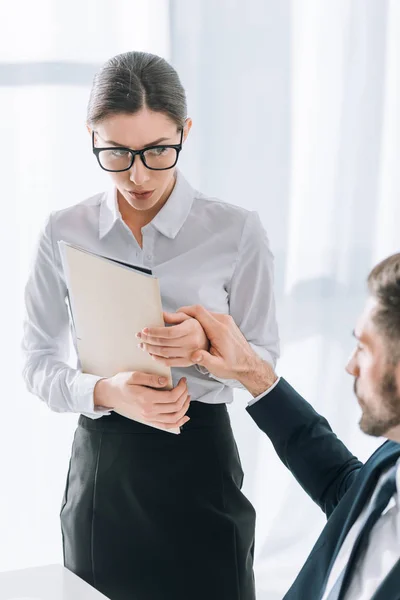 Cropped view of businessman touching hand of scared secretary in office — Stock Photo