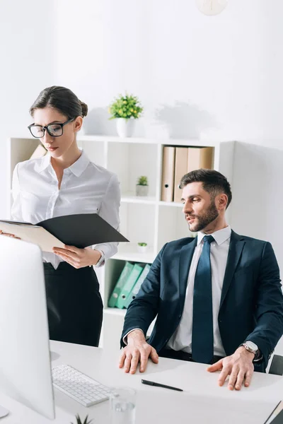 Hombre de negocios sentado en la mesa y mirando al secretario en la oficina - foto de stock