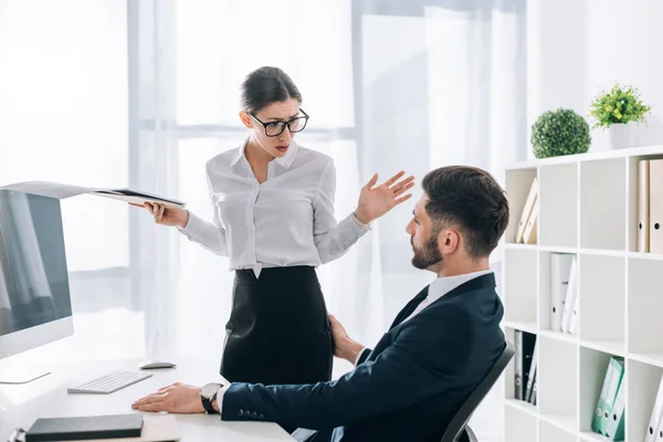 Hombre de negocios tocando el trasero de la secretaria conmocionada con carpeta en la oficina - foto de stock