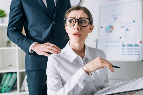 Cropped view of businessman touching shocked businesswoman in office — Stock Photo