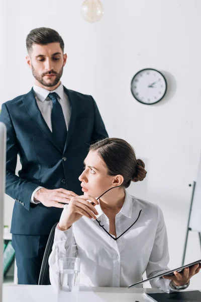 Guapo hombre de negocios en traje tocando impactada mujer de negocios en la oficina - foto de stock