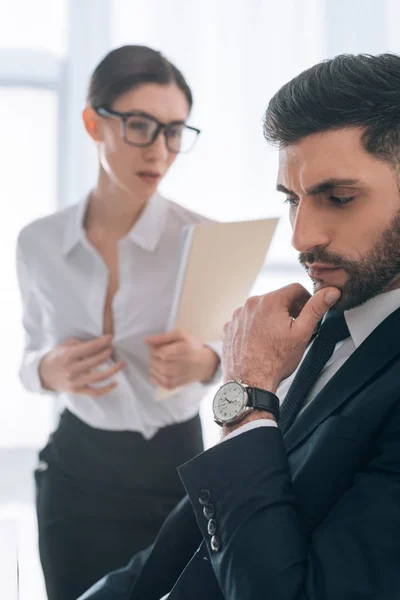 Selective focus of pensive businessman and secretary with big bust on background — Stock Photo