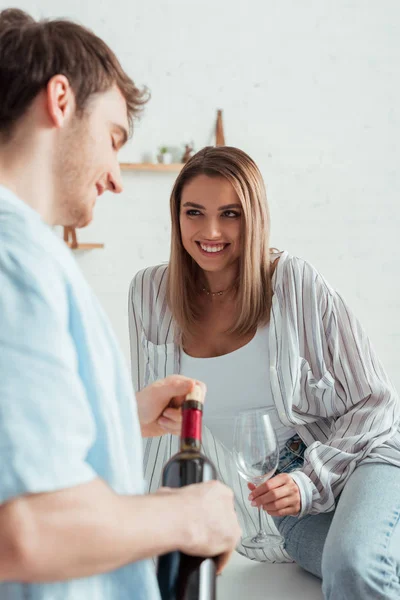 Foco seletivo da mulher olhando para o homem feliz segurando garrafa de vinho — Fotografia de Stock