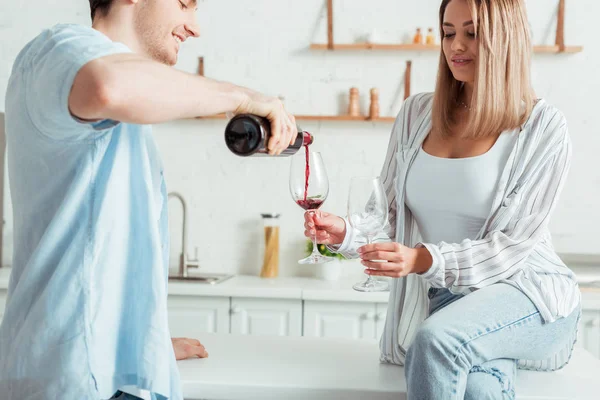 Homme gai verser du vin rouge dans le verre près de fille attrayante — Photo de stock