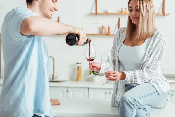 Fröhlicher Mann gießt neben attraktivem Mädchen Rotwein ins Glas — Stockfoto