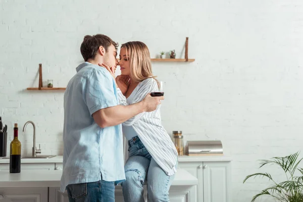 Hombre guapo sosteniendo copa de vino y besar a la mujer en casa - foto de stock