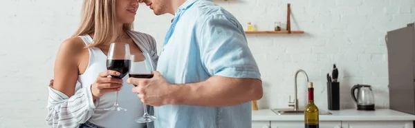 Panoramic shot of sexy couple holding wine glasses and kissing at home — Stock Photo