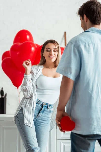 Man holding heart-shaped gift box near attractive girlfriend at home — Stock Photo