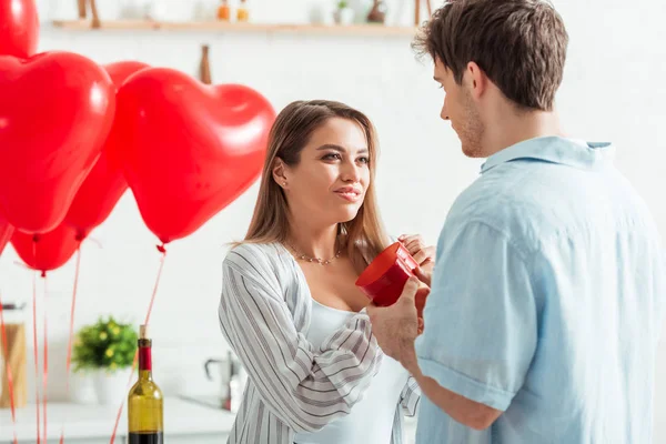 Man holding heart-shaped gift box near happy girlfriend on valentines day — Stock Photo