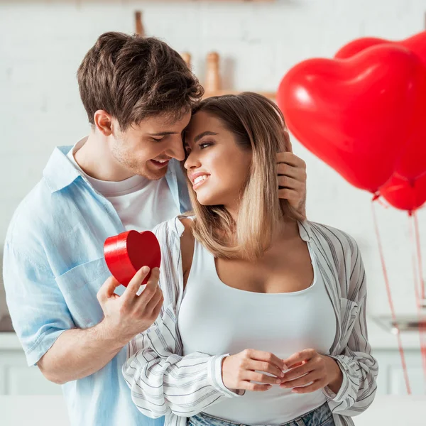 Mann mit herzförmigem Geschenkkarton und Blick auf fröhliche Freundin mit großer Brust — Stockfoto