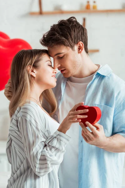 Side view of man holding heart-shaped gift box near beautiful girl — Stock Photo