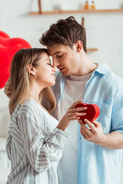 Vista lateral del hombre sosteniendo caja de regalo en forma de corazón cerca de hermosa chica - foto de stock