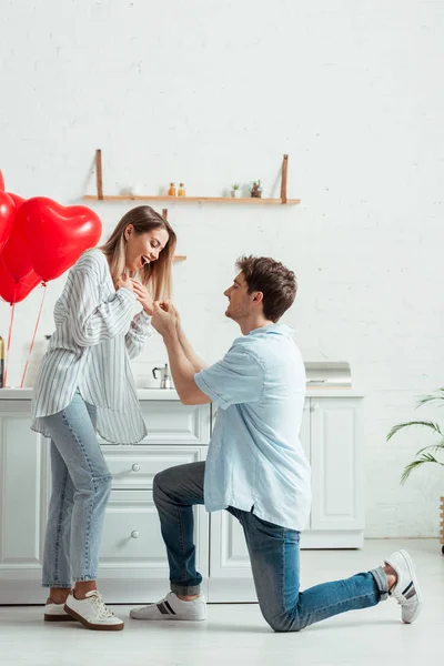 Glücklicher Mann steht auf Knien, während er der aufgeregten Frau zu Hause einen Heiratsantrag macht — Stockfoto