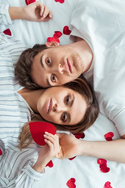 Vue de dessus de bel homme et belle femme couchée sur le lit près des cœurs rouges — Photo de stock