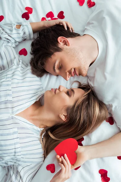 Top view of happy man and woman lying on bed near red hearts — Stock Photo