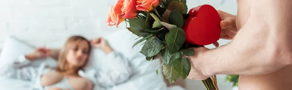 Panoramic shot of man with flowers and heart-shaped gift near seductive woman — Stock Photo