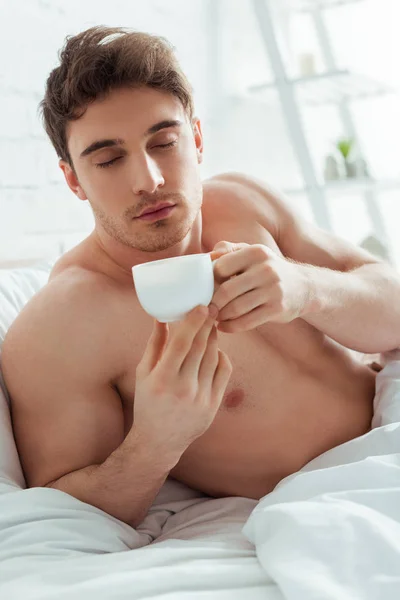 Uomo senza camicia con gli occhi chiusi in possesso di una tazza di caffè a letto — Foto stock