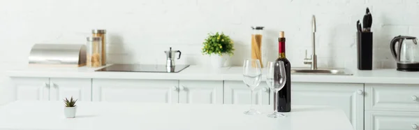 Панорамний знімок пляшки з червоним вином біля порожніх келихів на кухонному столі — стокове фото
