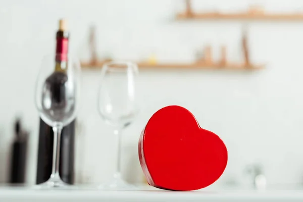 Fuoco selettivo della scatola regalo a forma di cuore rosso vicino a bicchieri vuoti e bottiglia di vino — Foto stock